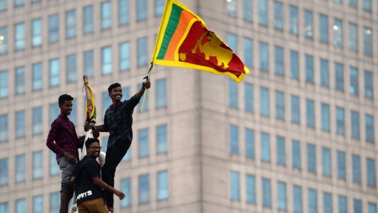 Um homem agita a bandeira nacional do Sri Lanka depois de subir em uma torre perto da secretaria presidencial em Colombo em 11 de julho de 2022, depois de ser invadida por manifestantes antigovernamentais. (Foto de Arun SANKAR/AFP)