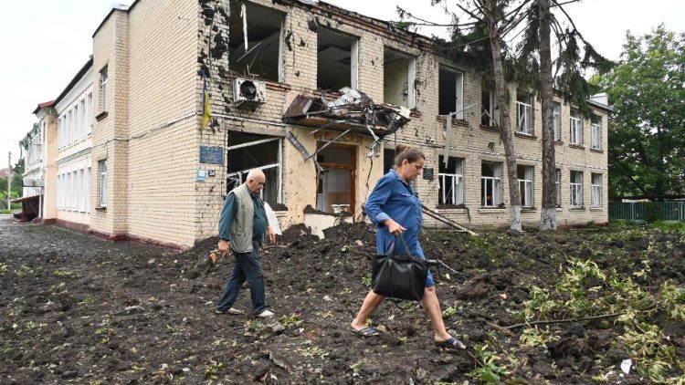 Moradores locais passam por um edifício danificado parcialmente destruído após um bombardeio na cidade de Chuguiv, a leste de Kharkiv, em 16 de julho de 2022. três pessoas na cidade de Chuguiv. (Foto de SERGEY BOBOK/AFP)