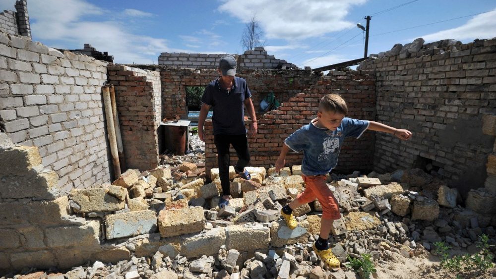 Um homem e uma crian?a caminham entre os escombros de uma casa, destruda durante batalhas nesta primavera na vila de Velyka Dymerka, a nordeste de Kyiv, em 21 de julho de 2022, em meio  invas?o russa da Ucr?nia. (Foto de Sergei CHUZAVKOV/AFP)