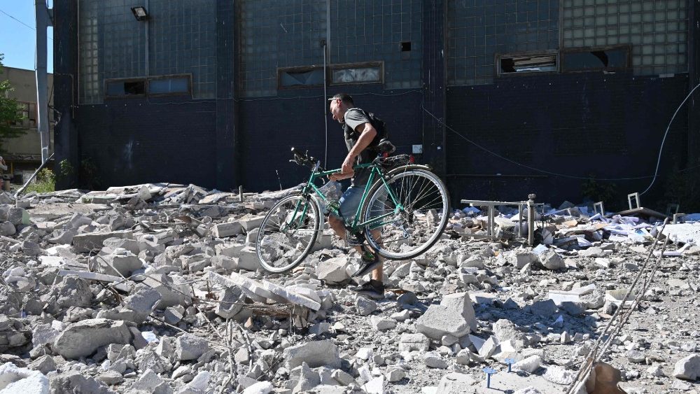 Um homem carrega sua bicicleta entre os escombros enquanto passa pela Press House, um complexo de uma grfica, escritrios editoriais e lojas em Kharkiv danificadas por um ataque de msseis na manh? de 31 de julho de 2022, em meio  invas?o russa da Ucr?nia. (Foto de SERGEY BOBOK/AFP)