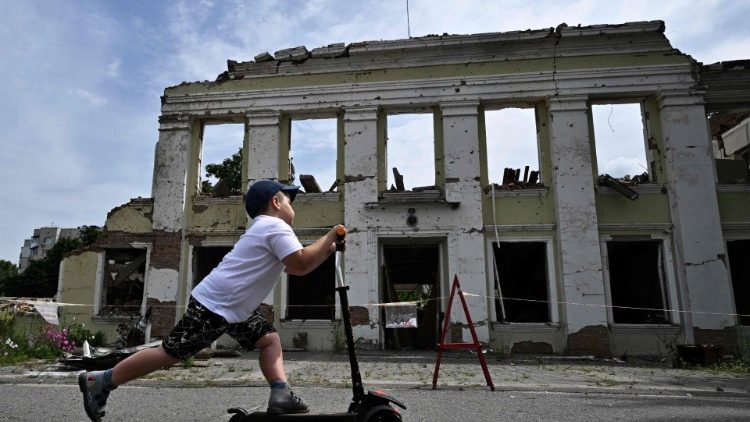 Um menino anda de scooter em frente ao prédio destruído da prefeitura na cidade de Okhtyrka, região de Sumy, em 1º de agosto de 2022. À medida que cidades e vilarejos em todo o interior da Ucrânia caíam diante da rápida invasão russa, Okhtyrka, uma cidade de 48.000 habitantes às margens do rio Vorskla, na região de Sumy, resiste à ocupação. (Foto de Genya SAVILOV/AFP)