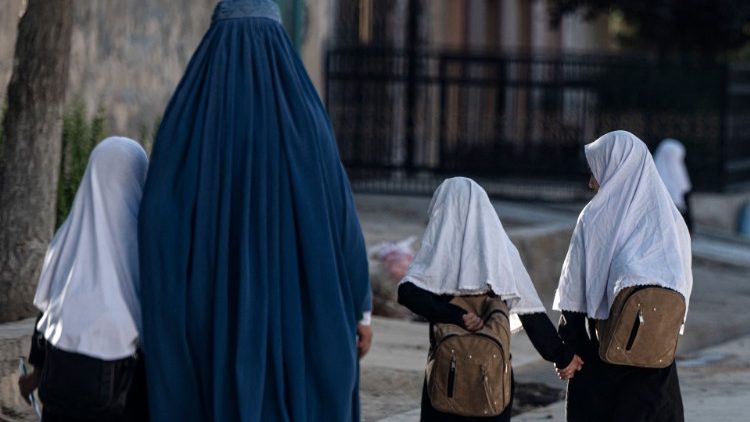 An Afghan woman walks with schoolgirls going to their primary school in Kabul