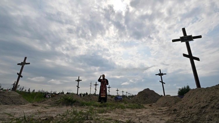 Sacerdote ortodoxo reza nos túmulos de civis não identificados durante funeral em um cemitério local na cidade de Bucha, região de Kyiv, em 11 de agosto de 2022. (Foto de Sergei SUPINSKY / AFP)