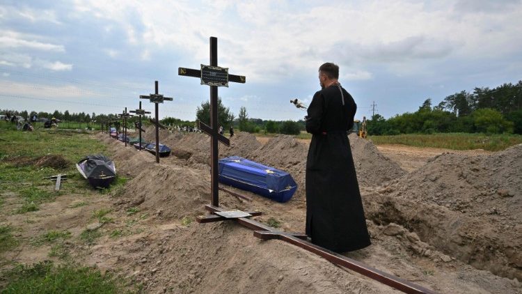 Sacerdote ortodoxo serve nos túmulos de civis não identificados durante funeral em um cemitério local na cidade de Bucha, região de Kyiv, em 11 de agosto de 2022. (Foto de Sergei SUPINSKY / AFP)