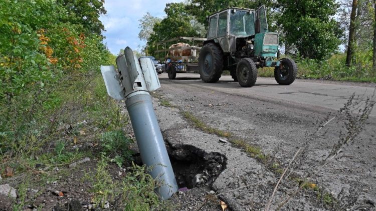Um trator passa pela cauda de um míssil que caiu na beira da estrada perto da cidade de Balakliya, região de Kharkiv, em 18 de setembro de 2022, recentemente recapturado pelo exército ucraniano após a retirada das tropas russas. (Foto por SERGEY BOBOK/AFP)