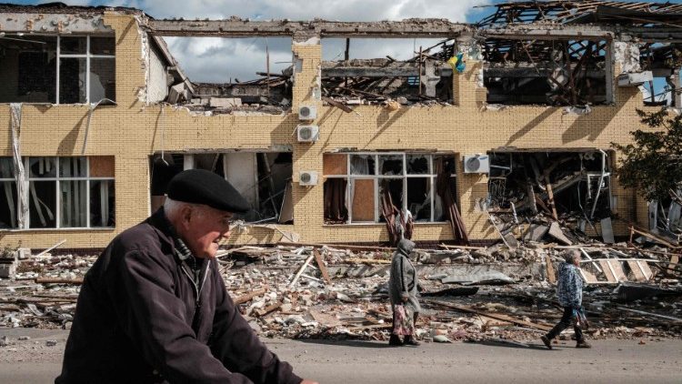 Pessoas passam por um prédio destruído em Kupiansk, região de Kharkiv, em 19 de setembro de 2022, em meio à invasão russa da Ucrânia. - Na cidade de Kupiansk, no nordeste, que foi recapturada pelas forças ucranianas, os confrontos continuaram com o exército russo entrincheirado no lado leste do rio Oskil. (Foto de Yasuyoshi CHIBA/AFP)