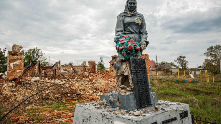 Nesta foto tirada em 26 de setembro de 2022, mostra um monumento aos que morreram durante a Segunda Guerra Mundial tendo como pano de fundo um prédio destruído durante a ocupação pelas tropas russas, na aldeia de Prudianka, região de Kharkiv, em meio à invasão russa de Ucrânia. (Foto de SERGEY BOBOK/AFP)