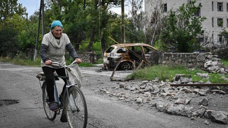 Uma mulher anda de bicicleta ao lado de um hospital local fortemente danificado na vila recentemente libertada de Vysokopillya, região de Kherson, em 27 de setembro de 2022, em meio à invasão russa da Ucrânia. (Foto de Genya SAVILOV / AFP)