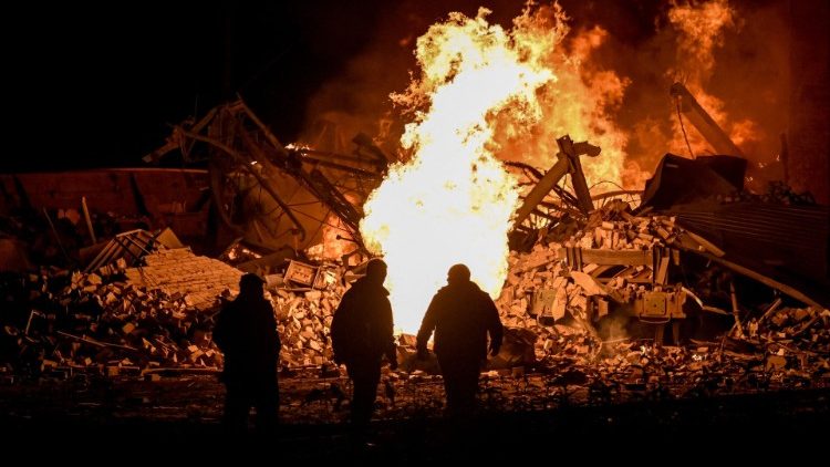 Bombeiros ucranianos ficam em frente às chamas quando um incêndio irrompeu em um depósito da estação ferroviária de carga em Kharkiv, que foi parcialmente destruída por um ataque de mísseis russos, em 27 de setembro de 2022, em meio à invasão russa da Ucrânia. (Foto de SERGEY BOBOK/AFP)