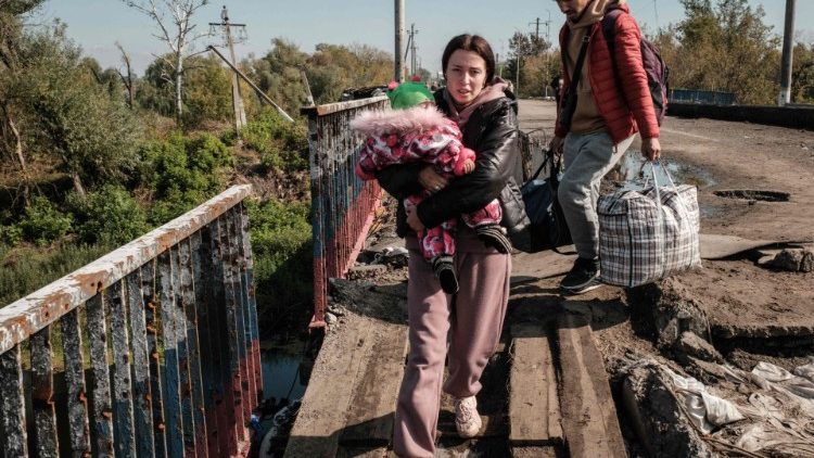 Viktoria Plotnykova, 20, segura sua filha Rita, de 9 meses, enquanto evacuam na ponte destruída sobre o rio Oskil em Kupiansk, região de Kharkiv, em 29 de setembro de 2022. (Foto de Yasuyoshi CHIBA / AFP)