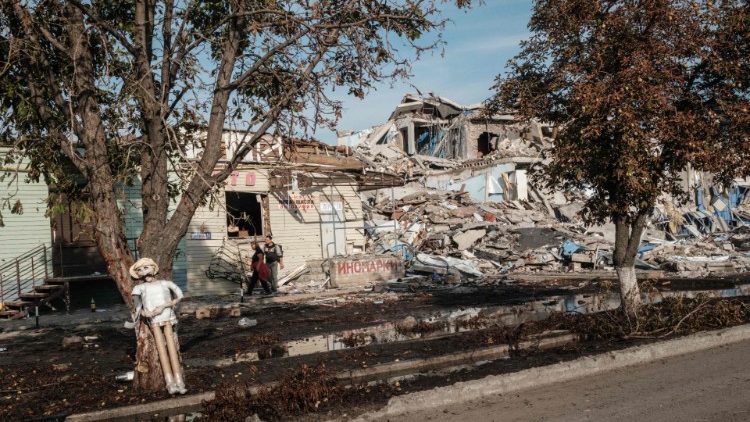 Moradores locais passam por lojas e casas destruídas na margem leste do rio Oskil, recentemente retomada, em Kupiansk, leste da Ucrânia, em 29 de setembro de 2022. (Foto de Yasuyoshi CHIBA / AFP)