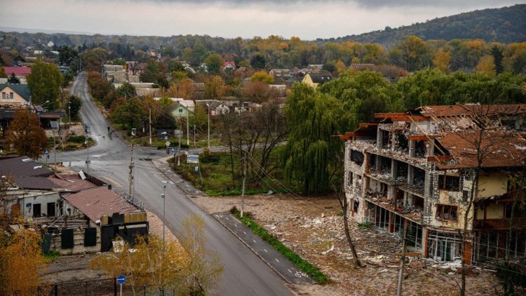 Moradores locais andam de bicicleta enquanto edifícios danificados são vistos em Svyatohirs'k, região de Donetsk, em 20 de outubro de 2022, após a liberação da área. (Foto de Dimitar DILKOFF/AFP)