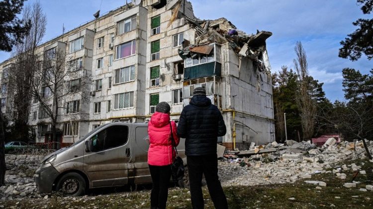Moradores locais observam um prédio residencial danificado por um ataque de míssil na vila de Kluhyno-Bashkyrivka, região de Kharkiv, em 2 de dezembro de 2022, em meio à invasão russa da Ucrânia. (Foto de SERGEY BOBOK / AFP)