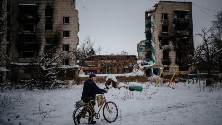 Residente local com sua bicicleta  em meio à neve, próximo a prédios bombardeados em Borodyanka, em 4 de dezembro de 2022. *AFP/Dimitar DILKOFF)