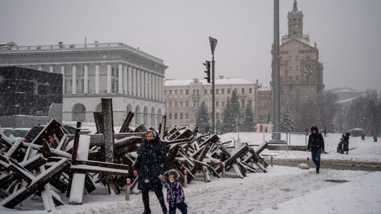Uma mulher e uma criança passam por estruturas antitanque cobertos de neve ao longo da Praça da Independência, na capital ucraniana, Kyiv, em 15 de dezembro de 2022, em meio à invasão russa da Ucrânia. (Foto de Dimitar DILKOFF / AFP)