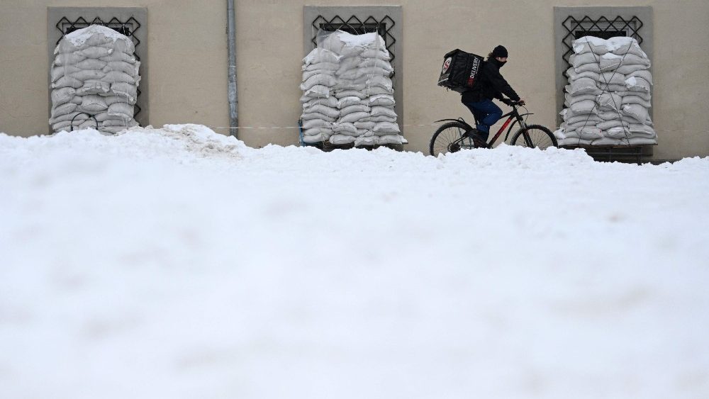 Um ciclista passa por sacos de areia cobertos de neve na cidade de Lviv, no oeste da Ucr?nia, em 7 de fevereiro de 2023, em meio  invas?o russa da Ucr?nia. (Foto de YURIY DYACHYSHYN / AFP)