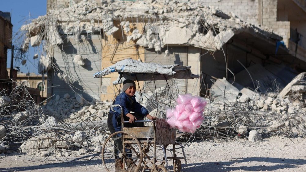 Uma crian?a sria que vende algod?o doce sorri em frente aos escombros de um prdio que desabou aps o terremoto da semana passada no vilarejo de Atarib, controlado por rebeldes na , na provncia de Aleppo, no noroeste, em 14 de fevereiro de 2023. (Photo by Aaref WATAD / AFP)
