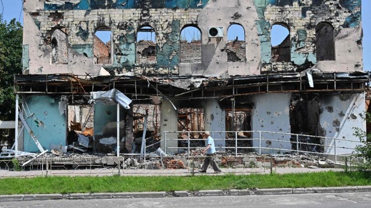 Um homem passa por prédios destruídos em Izyum, região de Kharkiv, em 27 de julho de 2023, em meio à invasão russa na Ucrânia. (Foto de SERGEY BOBOK / AFP)