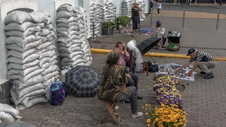 Mulheres vendem flores e outros itens em frente a sacos de areia que protegem as janelas de um prédio no bairro de Podil, em Kiev, em 30 de julho de 2023, em meio à invasão russa da Ucrânia. (Foto de Roman PILIPEY/AFP)