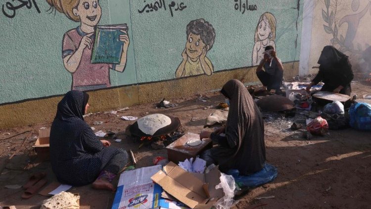 Palestinian women make traditional unleavened bread on an open fire at a shelter for displaced families mainly from the north of the Gaza Strip, at a UN-run school in Rafah, in the southern Gaza Strip