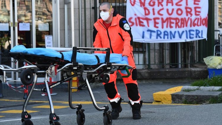 An Italian member of the White Cross in front of a banner expressing gratitude for health workers 