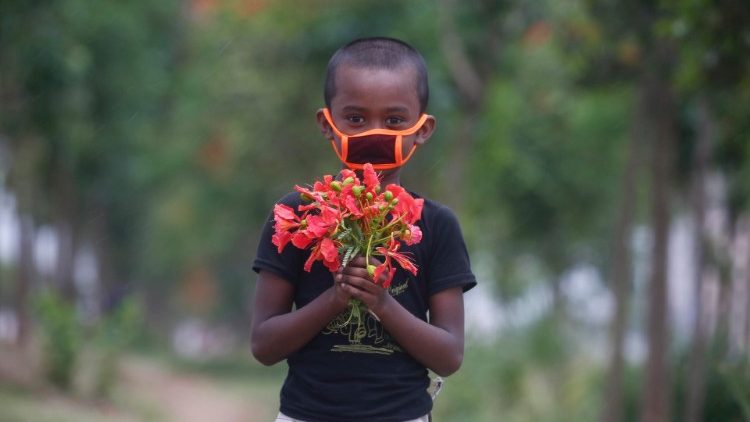 Menino protegido por máscara carrega flores em Daca, capital do Bangladesh