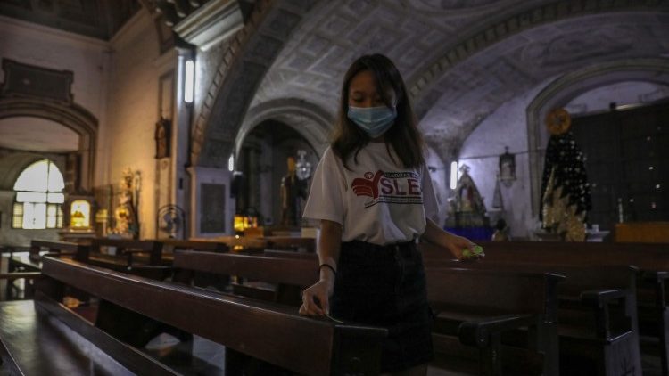 A volunteer puts social-distancing markers on a pew in a Manila church