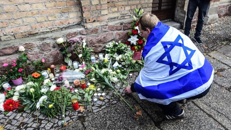 Um homem envolto em uma bandeira de Israel coloca flores em frente à sinagoga em Halle Saale, Alemanha, em 10 de outubro de 2019, após ataque de neonazista alemão, de 27 anos, que matou 2 pessoas