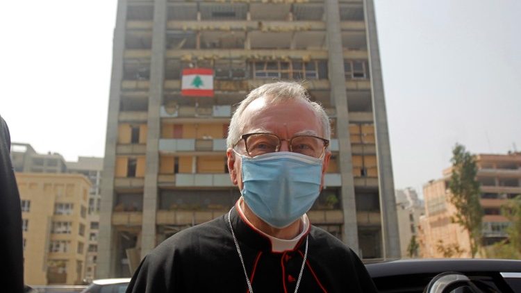 Kardinolas Parolinas lanko Beiruto jūrų uostą. Už jo nugaros - sprogimo nuniokoti namai