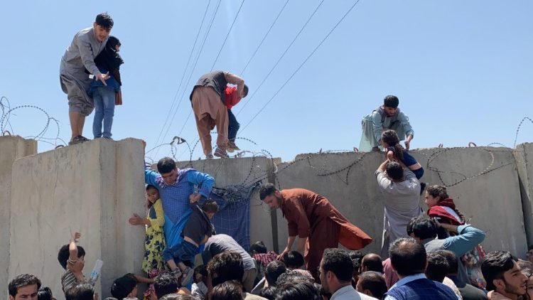 People struggling to cross the boundary wall at Kabul's international airport as the Taliban takes control of the city