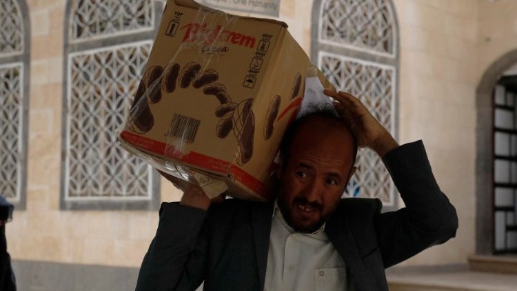 A Yemeni carries his child's monthly parcel of humanitarian food aid