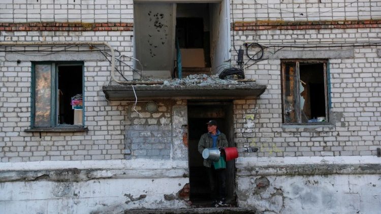 Um homem ucraniano carregando baldes para coletar água sai de uma casa danificada na cidade recentemente recapturada de Kupiansk, a leste de Kharkiv, nordeste da Ucrânia, em 15 de outubro de 2022. EPA/ATEF SAFADI