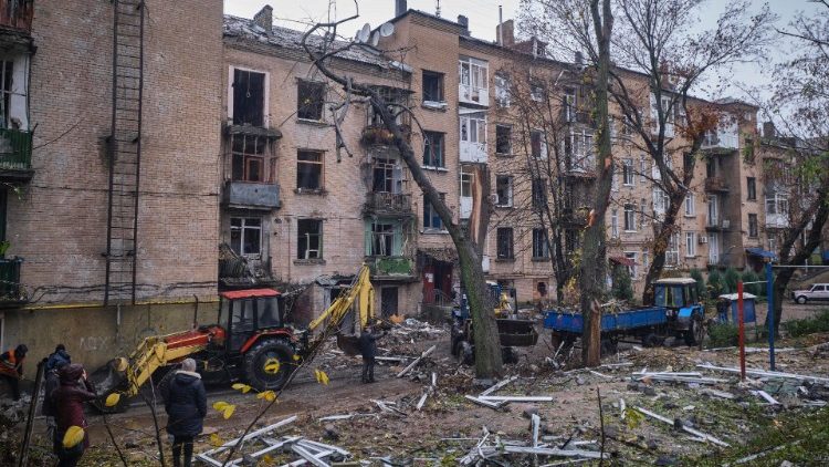 Moradores observam trabalhadores comunitários limparem os destroços de um prédio residencial danificado em um bombardeio noturno na pequena cidade de Druzhkivka, área de Donetsk, Ucrânia, em 26 de outubro de 2022, em meio à invasão russa. EPA/YEVGEN HONCHARENKO
