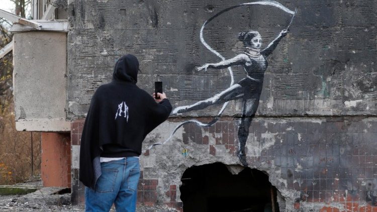 Pessoas assistem a um mural representando uma ginasta artística em um estilo semelhante às obras do artista de rua britânico Banksy, em uma parede de um prédio que foi destruído durante um bombardeio em Irpin, Ucrânia, 13 de novembro de 2022. Uma foto de um mural em Borodyanka representando uma ginasta foi compartilhado por Banksy em seu canal de mídia social em 11 de novembro, enquanto outros trabalhos atribuídos a ele em diferentes locais da Ucrânia e semelhantes ao estilo de Banksy ainda não foram compartilhados no canal do artista. As tropas russas entraram na Ucrânia em 24 de fevereiro de 2022, iniciando um conflito que provocou destruição e uma crise humanitária. EPA/SERGEY DOLZHENKO