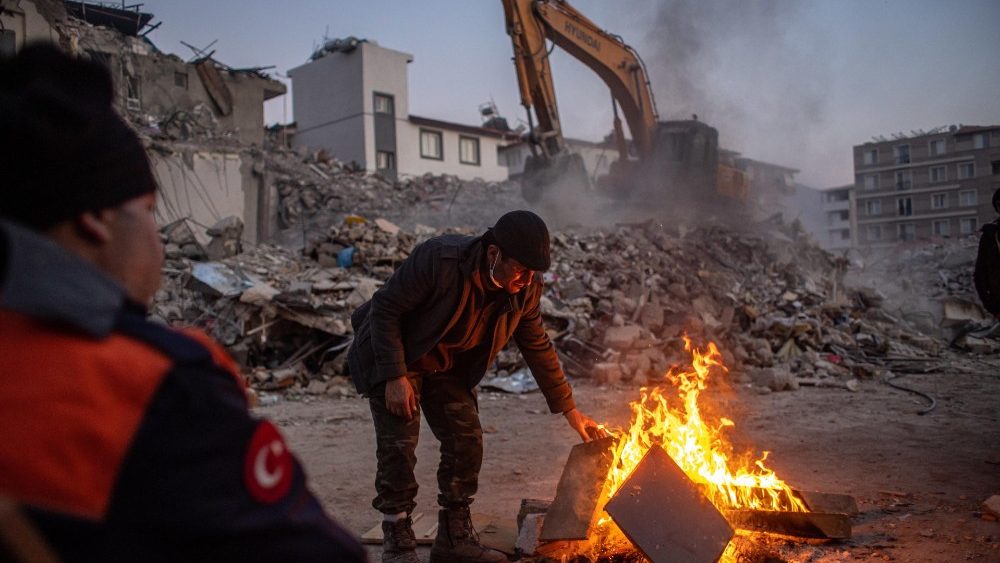 Um homem coloca lenha em uma fogueira perto do local de prdios desabados aps um forte terremoto, em Hatay, Turquia, 13 de fevereiro de 2023. EPA/MARTIN DIVISEK
