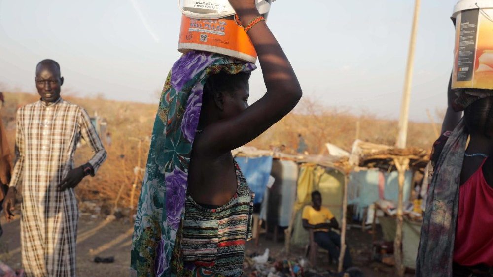 Pessoas que fugiram da violncia no Sud?o carregam recipientes de plstico em suas cabe?as enquanto passam pelo assentamento informal que cresce perto da rea de tr?nsito de refugiados e repatriados estabelecida pelo ACNUR na cidade de Renk, no estado do Alto Nilo, Sud?o do Sul, 11 de maio de 2023. EPA /AMEL DOR