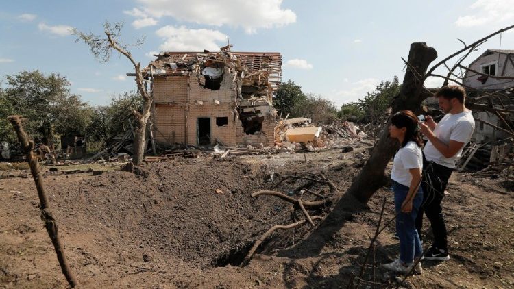 Pessoas olham para o buraco de bombardeio perto de um prédio privado destruído após um ataque com foguetes russos em sua vila de Rulykiv, perto de Kiev, Ucrânia, em 27 de agosto de 2023. EPA/SERGEY DOLZHENKO