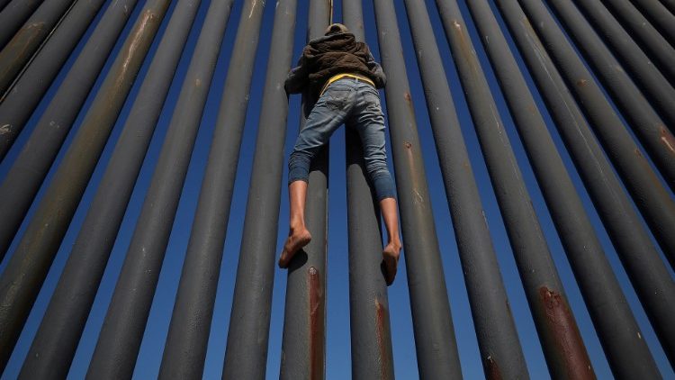 A migrant, part of a caravan of thousands from Central America, climbs the border fence between Mexico and the US 