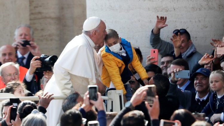 Pope Francis kisses a kid as he arrives for the weekly audience at the Vatican