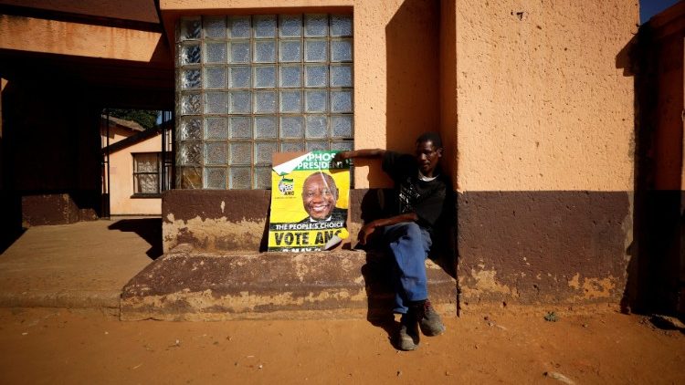 A supporter of President Cyril Ramaphosa's ruling African National Congress (ANC) sits beside a party poster as he awaits election results in Diepkloof township in Johannesburg