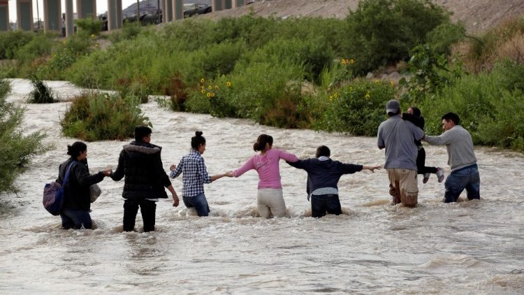 Migrants form a human chain to cross the Rio Bravo to enter into the United States