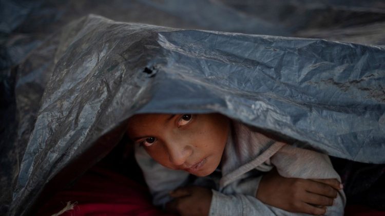 FILE PHOTO: Migrant boy from Honduras, part of a caravan of thousands trying to reach the U.S., looks out from under tarp at a shelter in Tijuana, Mexico