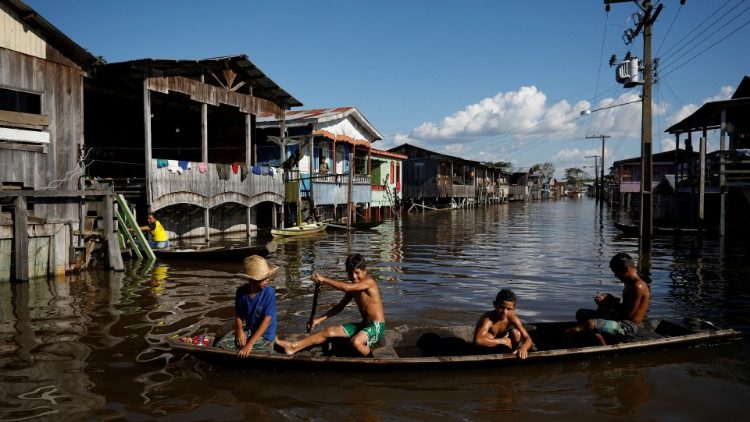 Children paddle their canoe through a street flooded by the rising Rio Solimoes, one of the two main branches of the Amazon River, in Anama