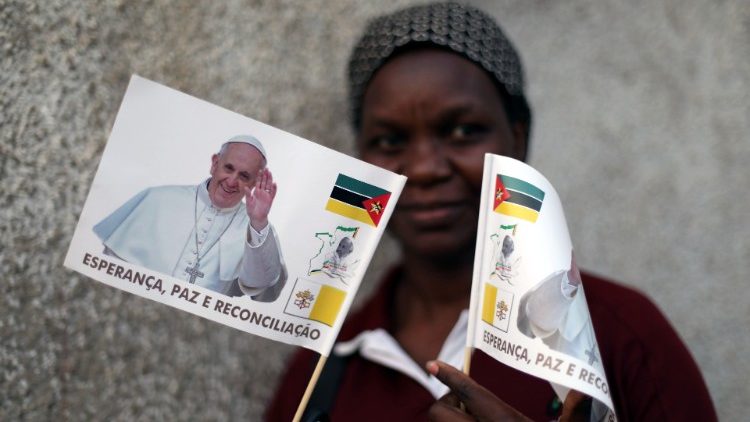 A women poses with flags bearing the face of Pope Francis outside a Catholic church in Lhanguene
