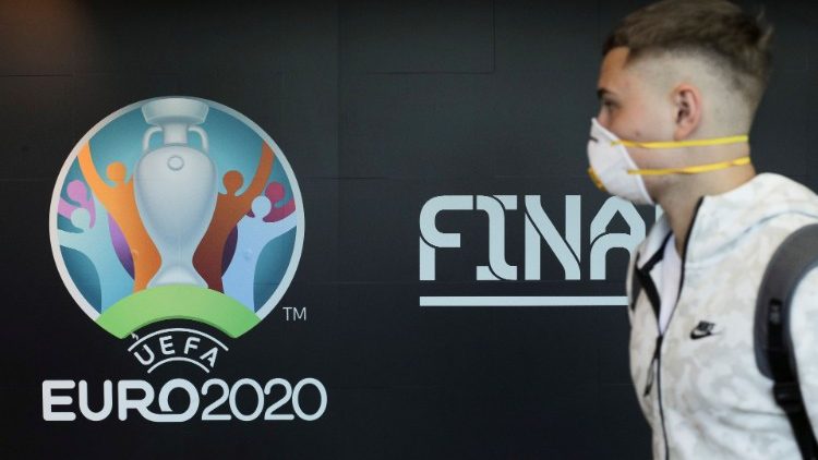 Travellers pass by a logo of the 2020 UEFA European Football Championship displayed on a wall inside Bucharest Henri Coanda International Airport