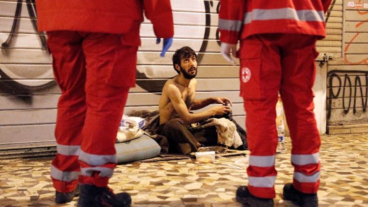 Zwei Rotkreuz-Helfer sprechen auf einer römischen Straße mit einem Obdachlosen