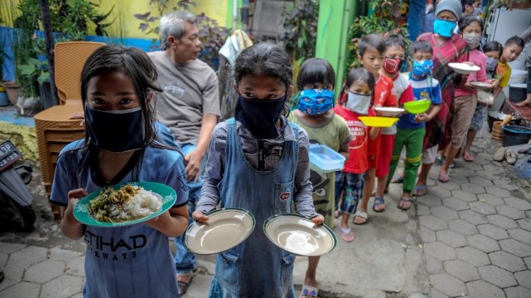 Locals wearing protective masks carry plates while queue for food distributed for free amid the spread of coronavirus disease (COVID-19) outbreak in Bandung