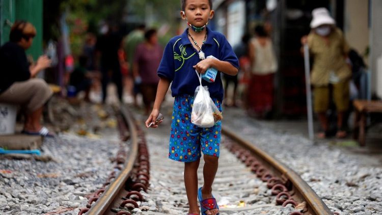 Menino caminha na linha férrea em Bangkok