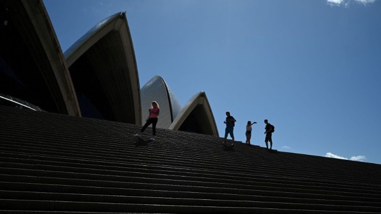 A handful of tourists stand atop the mostly deserted steps of the Sydney Opera House in Sydney