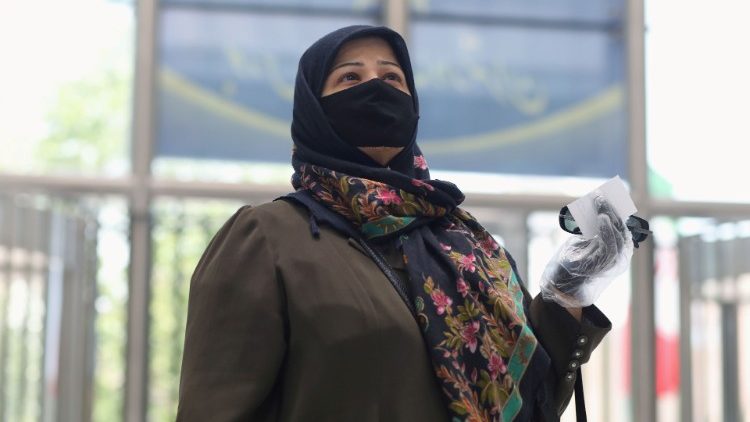 Une femme portant un masque et des gants de protection, regarde un tableau électronique indiquant le cours des actions, à la Bourse de Téhéran, le 8 juin 2020.